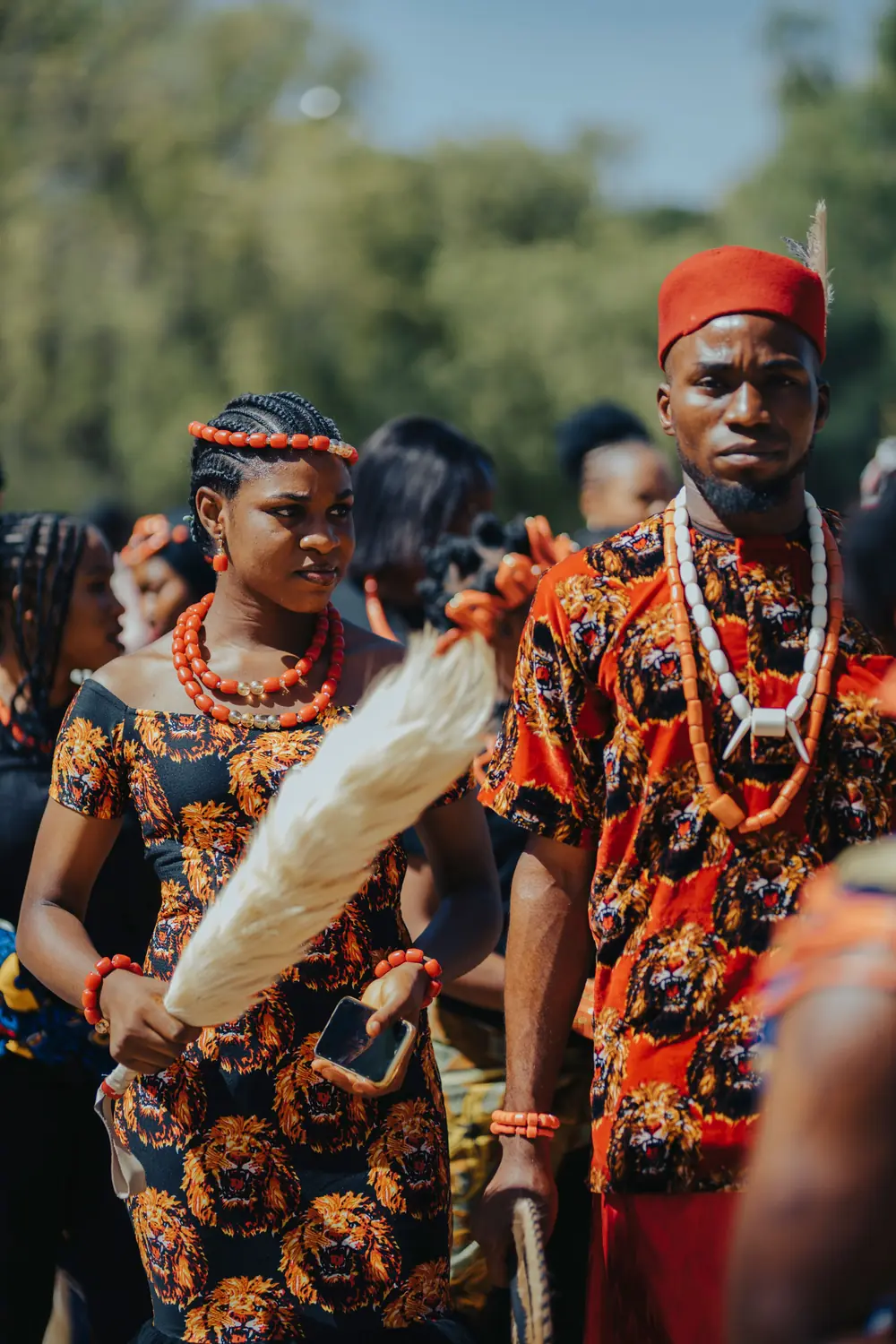 A young woman and man in lion print attire with coral and ivory beads